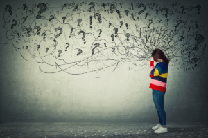 young woman standing in front of large wall with drawings of question marks representing her struggle to determine how does trauma affect the brain?