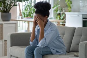 distraught woman seated on couch with head in her hands wondering can alcohol abuse worsen depression