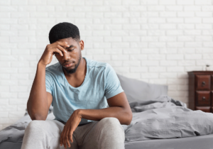 worried looking young man seated on his bed with his head in his hand wondering how does depression affect the brain