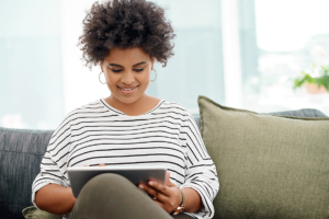 young woman seated on couch and using a tablet computer to answer the question is telehealth psychiatry right for you