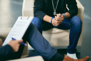 A man is leaning forward and speaking to a therapist about medication management.