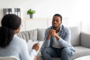 young man seated on couch in an office setting talking to a female mental health professional about why you should find an anxiety therapist in Silver Spring, MD.