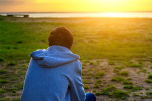 A man sits outside and enjoys the sunset, he is practicing alone time as a stress reduction technique on Thanksgiving.