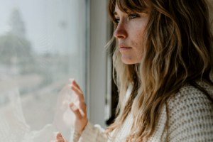 A woman stares out the window. Her social isolation is leading to loneliness.