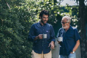 A man and his father are on a walk with their coffee mugs and engaging in healthy family communication.