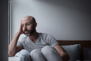 A man is sitting with his knees to his chest on a couch. He is experiencing severe depression.