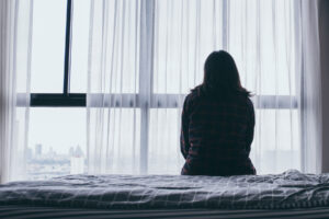 A woman sits in the dark, staring out the window. She is experiencing major depression disorder.