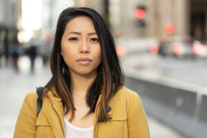 A woman is on a city street, standing face forward. She is thinking about committing a self-injurious behavior.