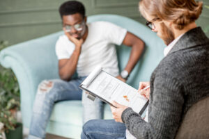 A young man in ripped jeans is getting therapy services in Woodbridge. He's sitting across from a therapist in an office.